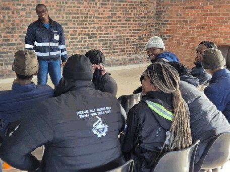 A Comodex facilitator leading an outdoor group session with delegates seated in branded mining workwear